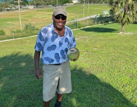 Man smiling outdoors holding a coconut.